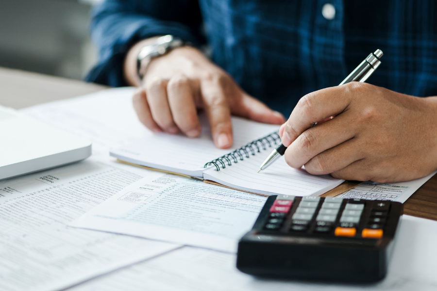 Un joven sostiene un bolígrafo mientras completa un documento y toma notas en un entorno profesional, representando el trabajo detallado y organizado propio de una asesoría fiscal y contable.