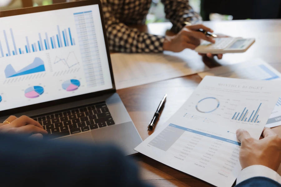 Profesionales analizando gráficos y datos económicos en un ordenador y documentos, representando cómo hacer un plan financiero para una empresa de forma estratégica y organizada.