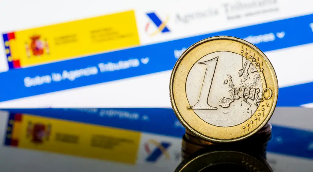 Moneda de 1 euro frente a pantalla de Agencia Tributaria en España, simbolizando Exenciones fiscales y gestión tributaria.