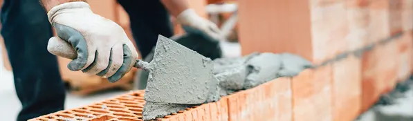 Trabajador colocando cemento sobre ladrillos en obra, simbolizando esfuerzo laboral y contexto de negociación o pacto salarial en construcción.